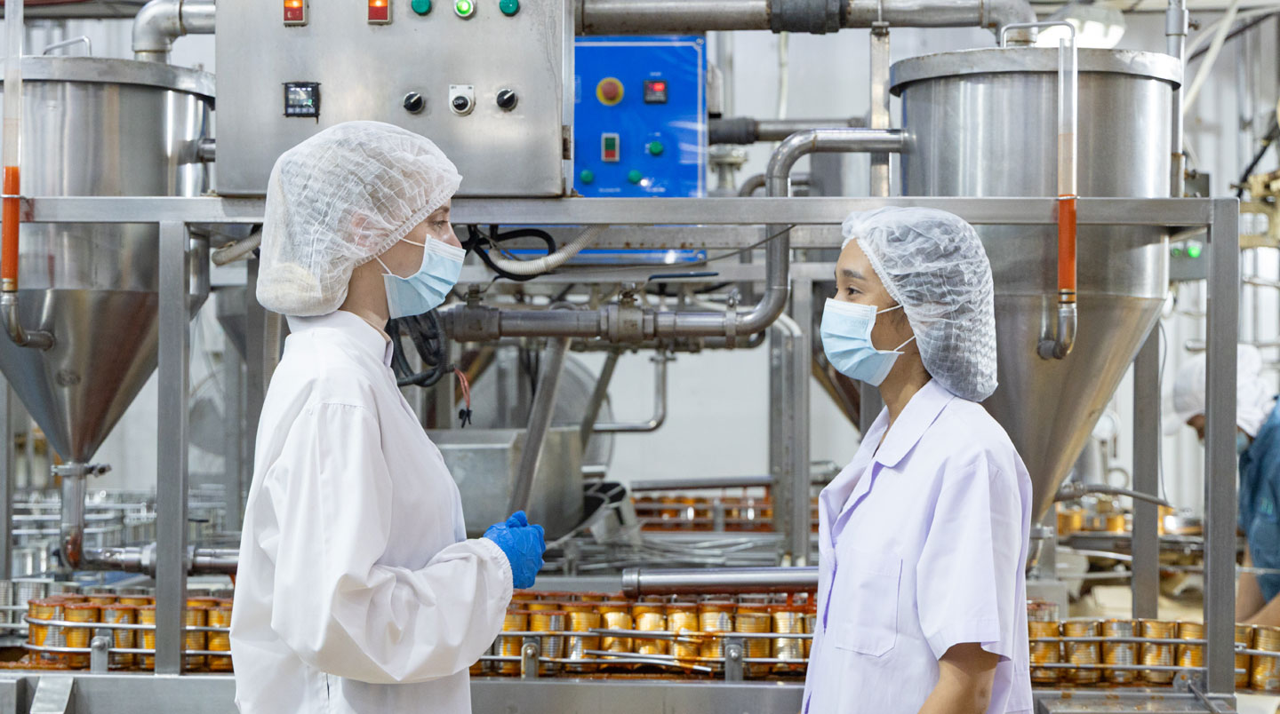 Produits extrudés salés en cours de séchage sur convoyeur inox sous panneaux émetteurs infrarouges céramiques, vapeur d'eau s'échappant des snacks capturée en contre-jour dans usine agroalimentaire